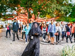 mulher trajada de uma típica viúva anda à frente de um grupo de pessoas na praça 15
