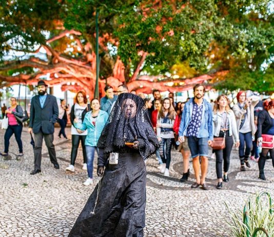mulher trajada de uma típica viúva anda à frente de um grupo de pessoas na praça 15