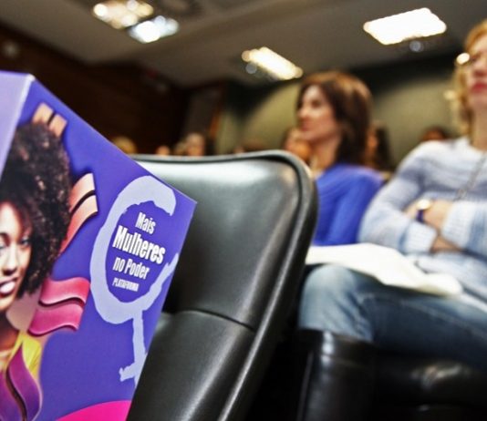 Somente em 2018, SC tem 1,4 mil estupros consumados cartilha da lei da maria da penha em primeiro plano sobre uma cadeira em auditório e mulheres sentadas ao fundo