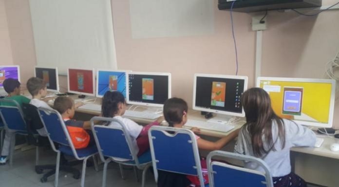 crianças vistas de costas sentadas a frente de computadores