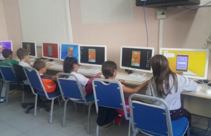 crianças vistas de costas sentadas a frente de computadores