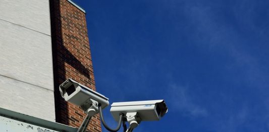 Novas tecnologias em segurança para São José visto de baixo, duas câmeras de segurança apontadas para direções diferentes em uma viga de aço ao redor de um prédio