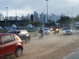 pista em curva cheia de serragem com alguns carros passando e caminhão tombado ao fundo