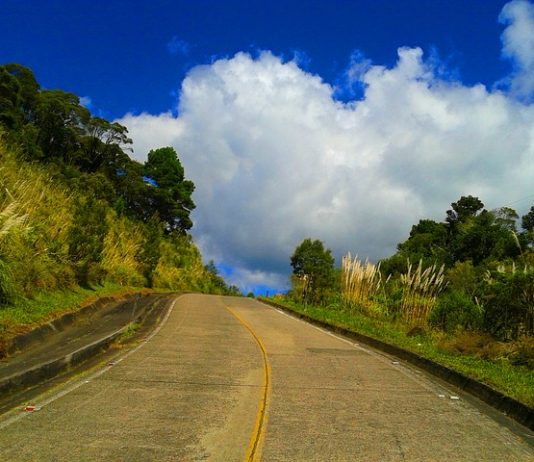Caminhos para o desenvolvimento estrada de cimento vista de baixo e do meio da pista que sobe um pequeno morro com árvores