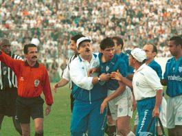 foto do clássico; margarida, de bigode e uniforme vermelho, gesticula com o braço, enquanto membros da equipe técnica do avaí seguram um jogador revoltado