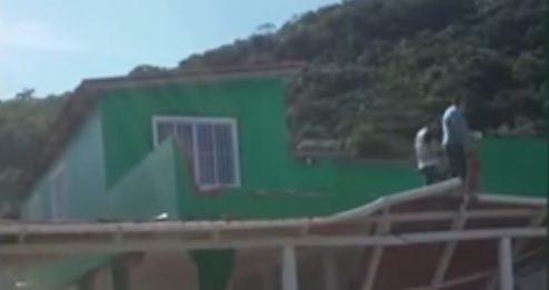 casa verde de dois andares sendo demolida na parte frontal; há partes do telhado no chão