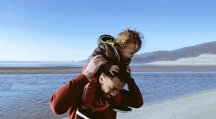 homem segura criança acima da cabeça "no cavilho" em uma paisagem de praia