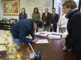 Empossados novos servidores em São José homem se abaixa para assinar um documento em uma mesa na frente da prefeita adeliana e mais algumas pessoas ao fundo em pé observam