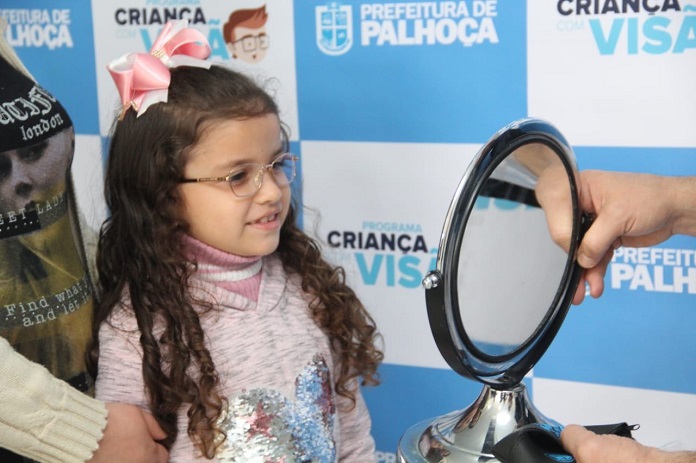 garota de aproximadamente 7 anos olha sorridente para um espelho usando óculos