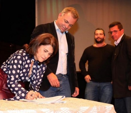 Lançado o 23° festival de teatro Isnard Azevedo mulher assina documento em cima de uma mesa e ao lado o prefeito gean loureiro observa; há outros dois homens atrás