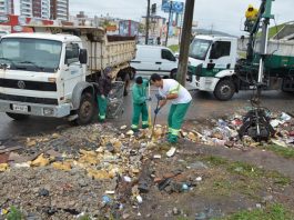 dois funcionários da comcap recolhem lixo com pás ao lado de dois caminhões da companhia