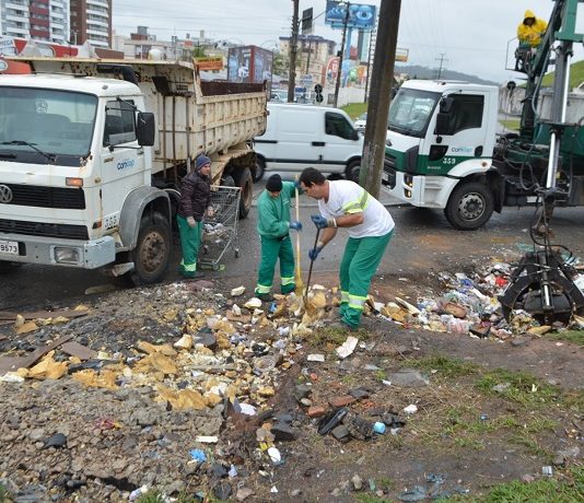 dois funcionários da comcap recolhem lixo com pás ao lado de dois caminhões da companhia