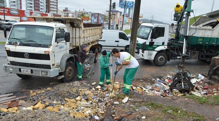 dois funcionários da comcap recolhem lixo com pás ao lado de dois caminhões da companhia