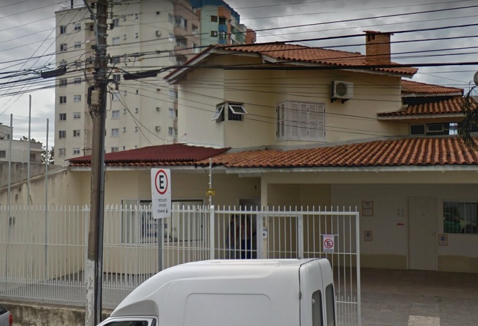fachada da casa sede do igp em são josé; portão de grade e um poste na frente com muitos fios; alguns carros estacionados