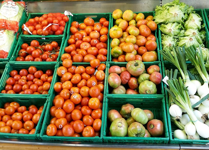 estande de legumes em supermercado com tomates de diversos tamanhos e outros legumes