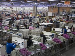 linha industrial de costura vista de cima com dezenas de trabalhadoras uniformizadas em cada posto