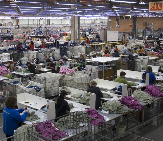 linha industrial de costura vista de cima com dezenas de trabalhadoras uniformizadas em cada posto