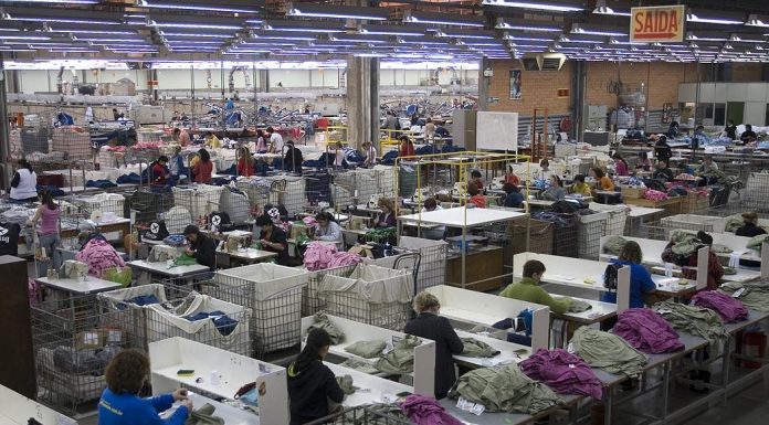 linha industrial de costura vista de cima com dezenas de trabalhadoras uniformizadas em cada posto