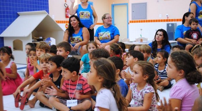 turma de crianças de cerca de 7 anos sentada no chão assistindo aula