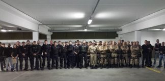 grupo de policias, entre guarda municipais, militares e civis, posa em linha para foto em uma grande garagem