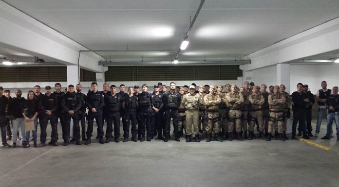 grupo de policias, entre guarda municipais, militares e civis, posa em linha para foto em uma grande garagem