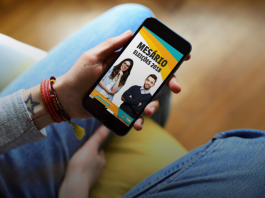 pessoa segura um celular onde há imagem na tela com um homem e uma mulher e está estrito "mesário"