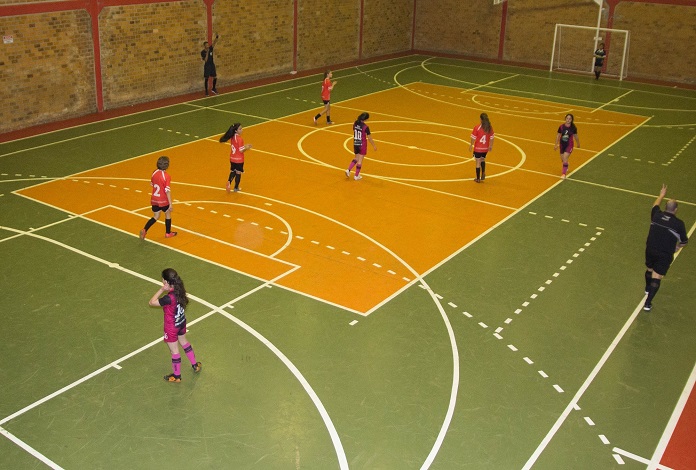 quadra de futsal onde estão jogando dois times de meninas