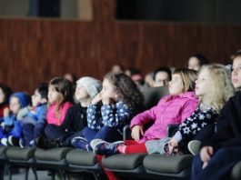 Mostra de Cinema Infantil: confira a programação de julho no CIC crianças em uma fileira de poltronas de cinema assistindo a um filme com os rostos iluminados pela tela; olha na mesma direção