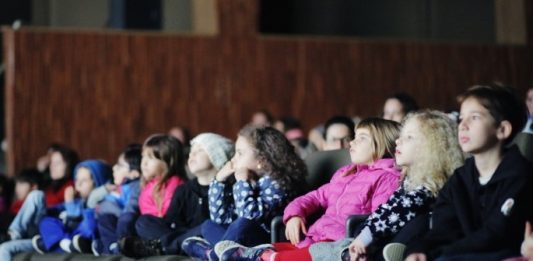 Mostra de Cinema Infantil: confira a programação de julho no CIC crianças em uma fileira de poltronas de cinema assistindo a um filme com os rostos iluminados pela tela; olha na mesma direção
