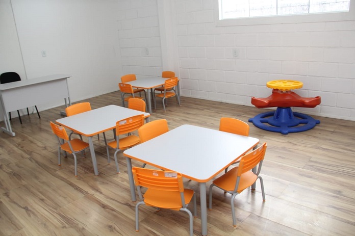 sala de aula com duas mesas infantis cercadas por cadeiras laranjas para crianças e alguns brinquedos