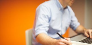 homem em frente ao notebook anota com uma caneta em um papel