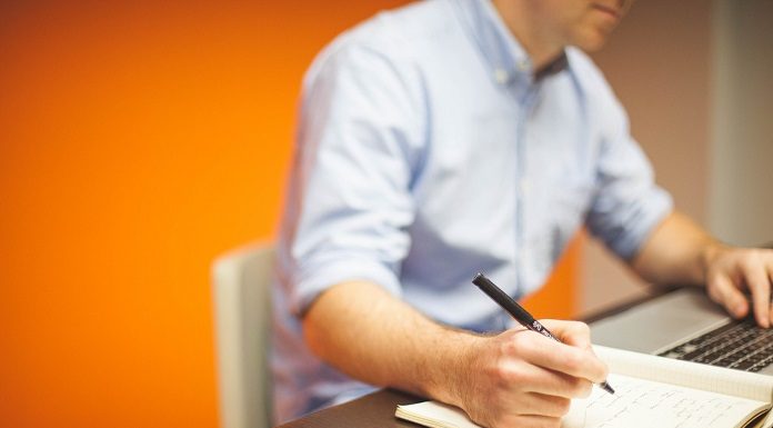homem em frente ao notebook anota com uma caneta em um papel