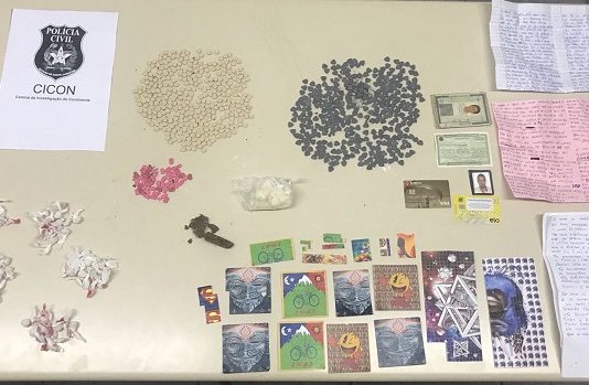 mesa de escritório com todas as drogas apreendidas dispotas; são pequenos montes de pílulas, cartelas e embalagens de plástico