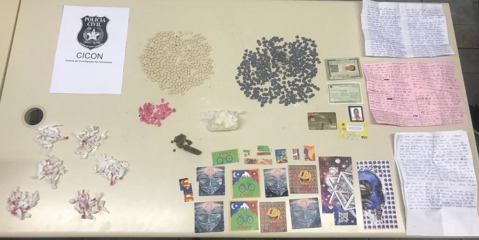 mesa de escritório com todas as drogas apreendidas dispotas; são pequenos montes de pílulas, cartelas e embalagens de plástico