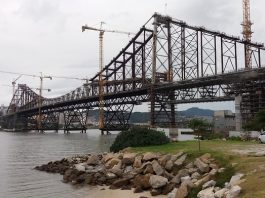 ponte hercílio luz vista da cabeceira continental em construção em dia nublado; há guindastes ao longo da estrutura