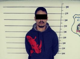 Liderança do PGC é presa ao ir à academia em Palhoça homem com o rosto censurado diante do quadro de medição de altura na delegacia posa para foto usando moletom