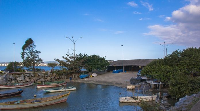 trecho de mar com pequenos barcos ancorados em frente a uma rampa de acesso aos ranchos, com árvores em volta