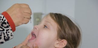 garota abre a a boca para recebe as gotinhas de vacinação