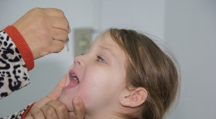 garota abre a a boca para recebe as gotinhas de vacinação
