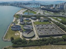 Duas grandes obras de esgotamento são anunciadas para a Capital imagem aérea de uma estação de tratamento de esgoto em área na beira do mar no centro de florianópolis, onde ao fundo é possível ver prédios e as pontes em dia de sol