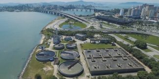 imagem aérea de uma estação de tratamento de esgoto em área na beira do mar no centro de florianópolis, onde ao fundo é possível ver prédios e as pontes em dia de sol