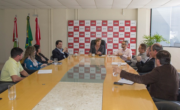 prefeita sentada na ponta de uma grande mesa conversando com secretários em volta