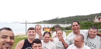 professor faz selfie com grupo de alunos da apae usando a camisa do projeto em área externa próxima ao mar