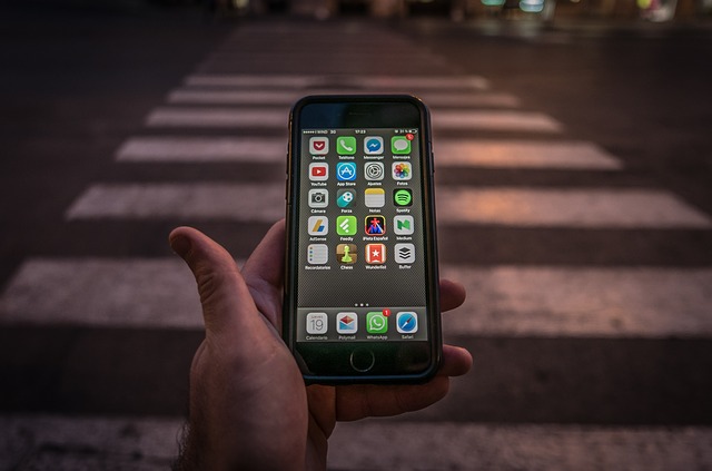 close em uma mão que segura um celular com tela ligada mostrando aplicativos; pessoa está em frente a uma faixa de pedestre