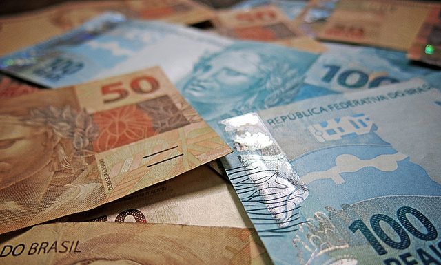 notas de 50 e 100 reais dispostas sobre uma mesa