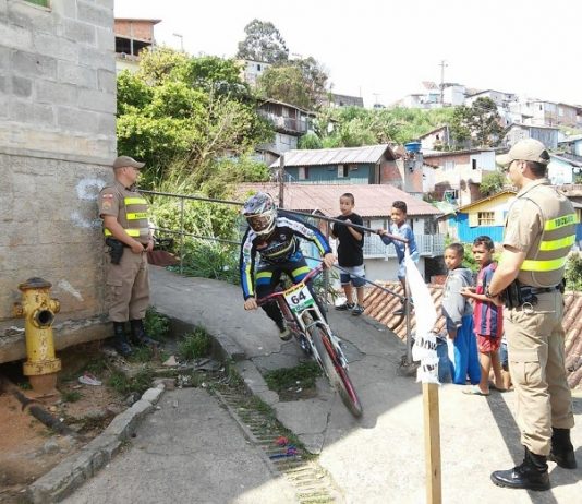 piloto faz uma curva de um caminho do morro observado por dois pm e um grupo de crianças ao lado