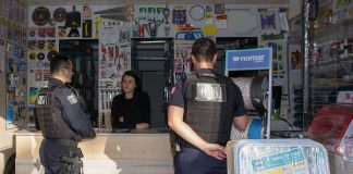 dois guardas conversam com uma mulher atrás de um balcão de um comércio de ferramentas