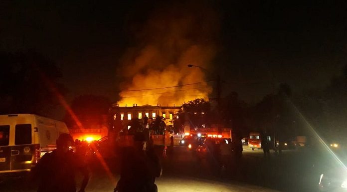 foto noturna da fachada do prédio histórico em chamas; algumas silhuetas de agentes de segurança na frente