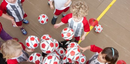 No sábado (15) tem aula de inglês e futebol grátis para crianças crianças pequenas com o mesmo uniforme tentam pegar bolas de um monte, vistas de cima em uma quadra