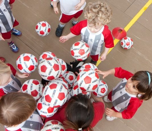 No sábado (15) tem aula de inglês e futebol grátis para crianças crianças pequenas com o mesmo uniforme tentam pegar bolas de um monte, vistas de cima em uma quadra